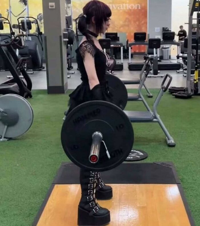 A person dressed in gothic occult style lifting weights in a gym, blending fitness with occult aesthetics.