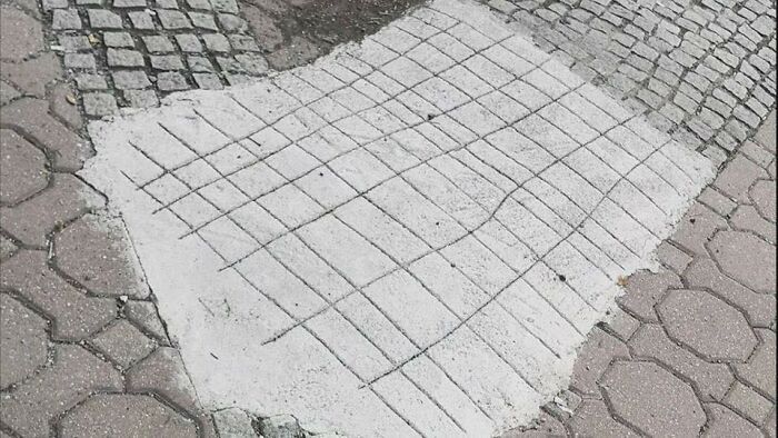 Patch of concrete on cobblestone with grid lines and curved accents, showcasing pleasures of the occult in an unexpected setting