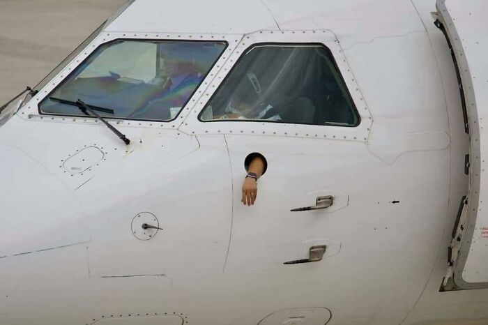 Airplane cockpit with an arm sticking out of a small window, illustrating hilarious pleasures of the occult moments.