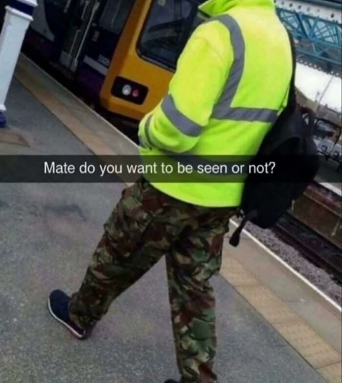 Person wearing a high-visibility jacket and camouflage pants at a train station, humorously questioning visibility in pleasures of the occult.