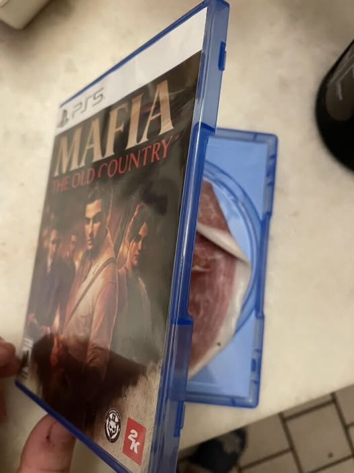 PS5 game case for Mafia The Old Country shown opened with a slice of ham inside, illustrating humorous out of context pleasures of the occult.