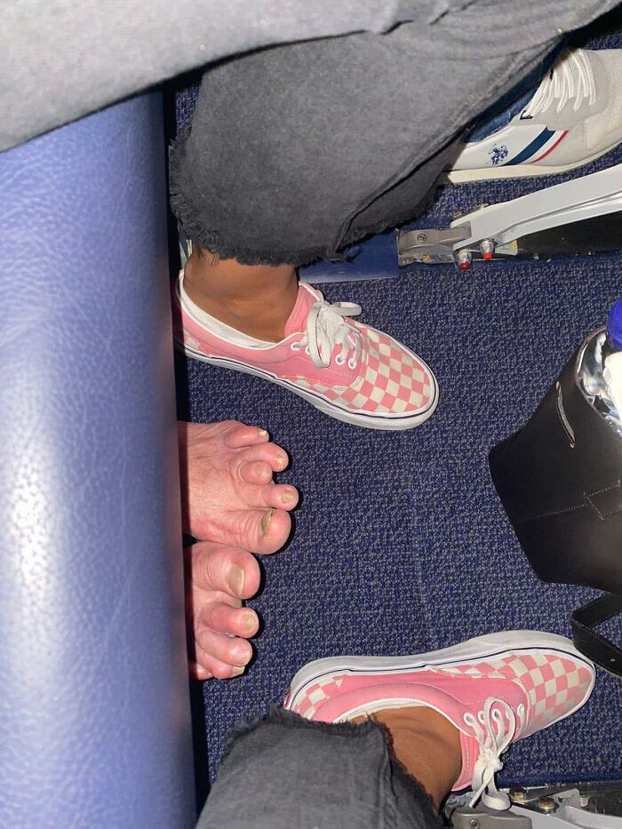 Bare feet and pink checkered sneakers on airplane floor creating an out of context moment for pleasures of the occult.