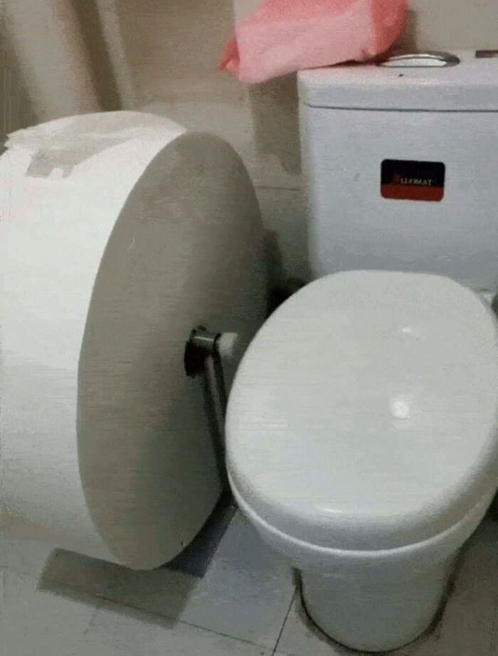 Oversized toilet paper roll mounted next to a toilet, creating a humorous and out of context bathroom scene.
