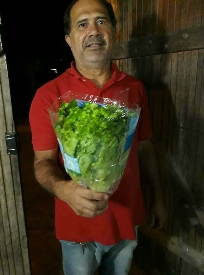 Man in red shirt holding a bouquet of lettuce wrapped in plastic, creating a humorous occult-themed out of context moment.