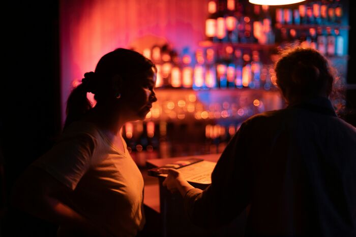 Two people in a dimly lit bar, with one holding a menu, illustrating a painful table for two moment from waiters.