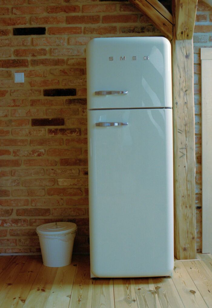 Retro fridge in a kitchen with brick walls and wooden floor, illustrating bizarre things found inside strangers’ houses.