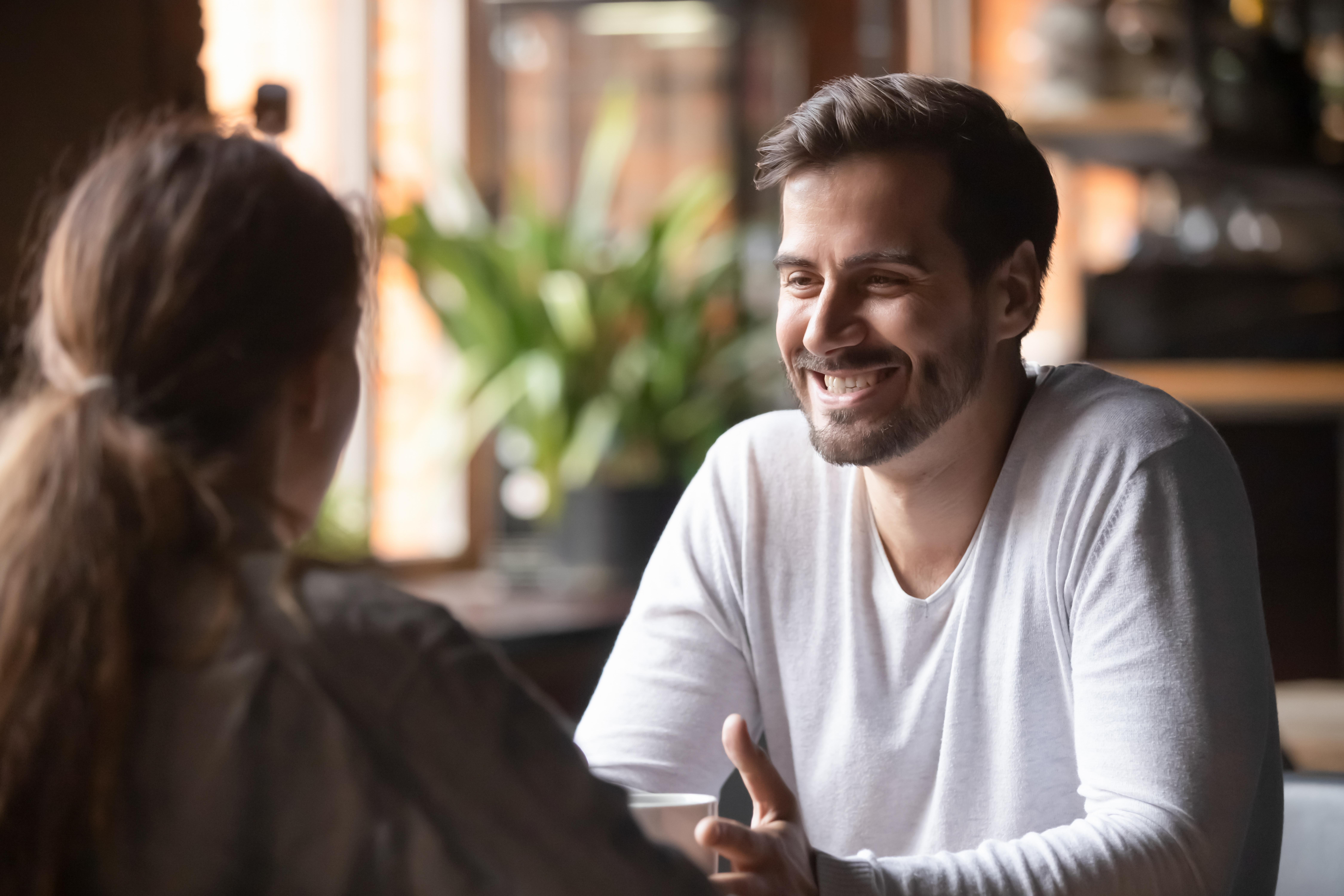 Man smiling and talking to woman in cafe, relating to GF resuming shaving and wearing makeup beauty routine.