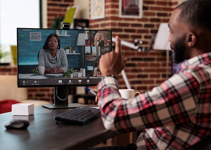Man in plaid shirt engaging in a virtual meeting, contemplating exposing management and HR to coworkers.