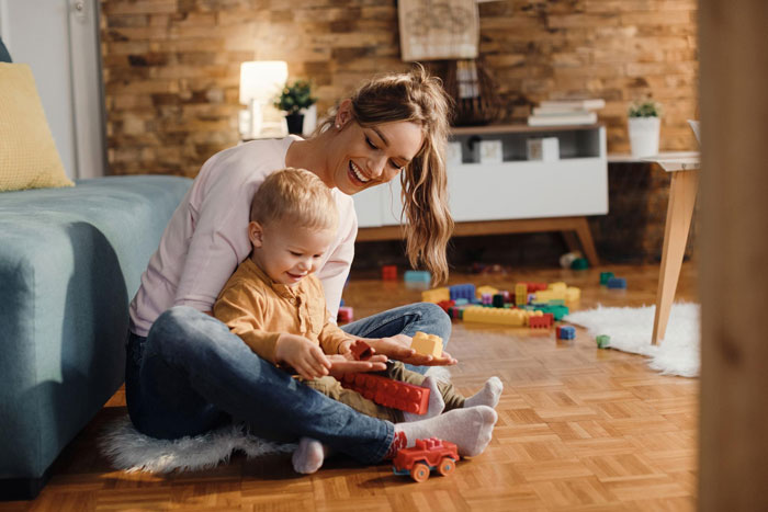 Young child playing with toys on the floor with smiling bio mom in cozy living room, highlighting kids prefer bio mom. Young child playing with toys on the floor with smiling bio mom in cozy living room, highlighting kids prefer bio mom.