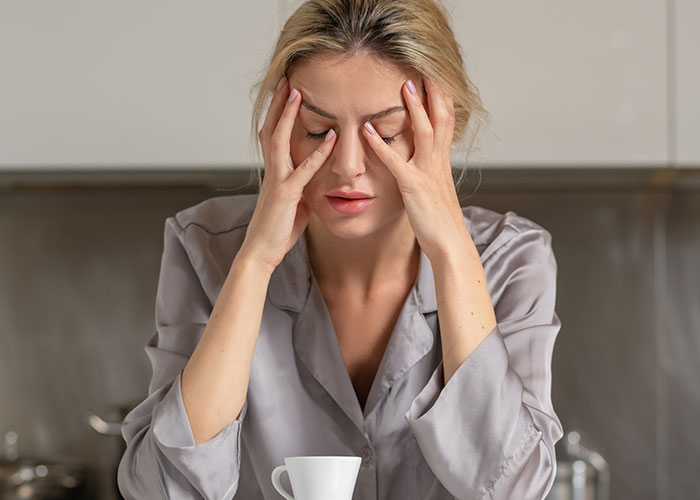 Woman stressed at work, holding head with closed eyes, feeling awkward after stopping baking for colleagues over nickname.