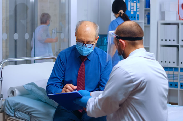 Elderly patient in hospital room consulting doctor about refusing donate liver lawsuit while wearing a protective mask.