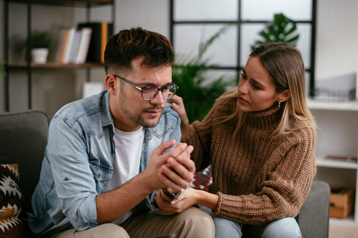Man looking worried while woman wearing brown sweater comforts him discussing refusing donate liver lawsuit issues at home