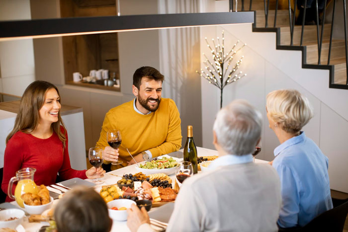 Group of family members enjoying Thanksgiving dinner with wine and food, highlighting holiday gathering at home.