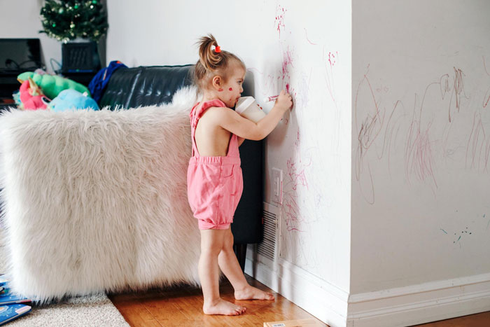 Toddler drawing on a wall in a messy living room, highlighting family stress and house damage after Thanksgiving hosting.