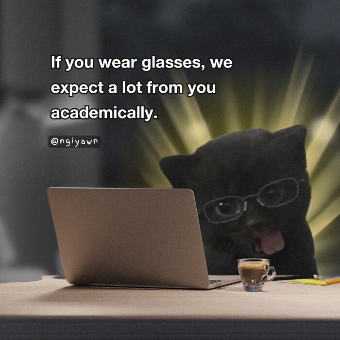 Black cat wearing glasses behind a laptop with coffee, illustrating relatable cat memes about academic expectations.