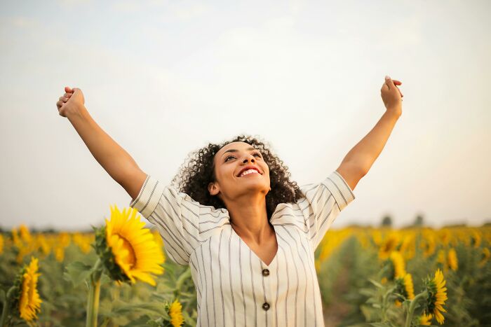 Woman in sunflower field raising arms joyfully, symbolizing infinite happiness and luck in life choices.