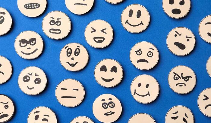 Round wooden tokens with various hand-drawn facial expressions representing emotions like happiness and anger on a blue background.