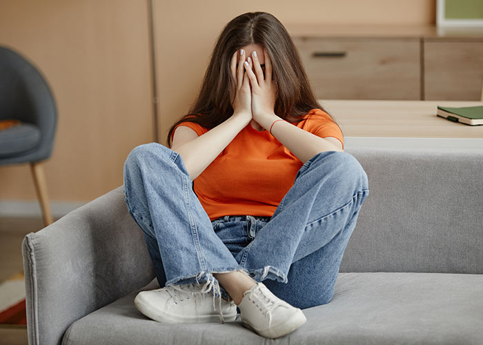 Young woman in orange shirt sitting on couch upset over rich boyfriend demands equal split rent refused
