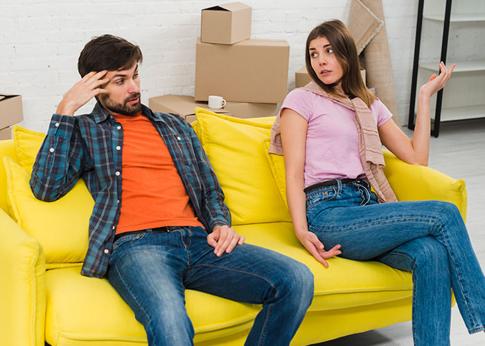 Young rich boyfriend and girlfriend sitting on yellow couch arguing about equal split rent during move.