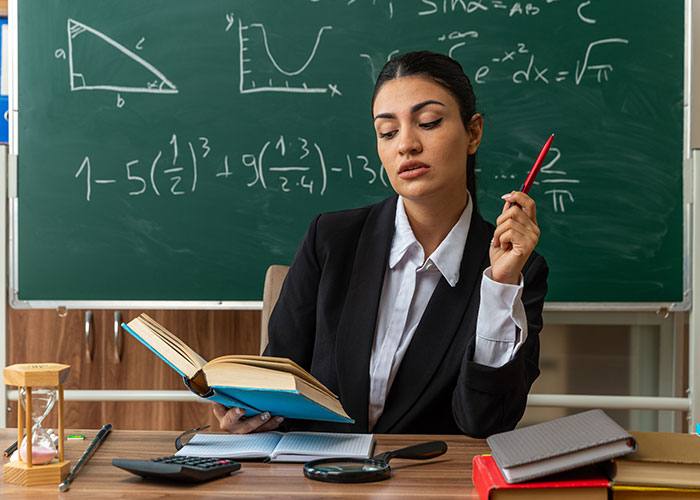 Woman in black suit holding a book and pen, sitting in front of a chalkboard with math formulas, symbolizing rich boyfriend demands split rent.