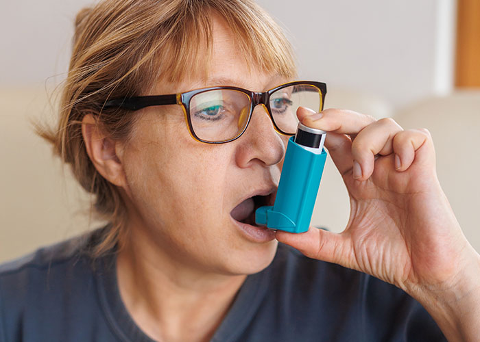 Woman using an inhaler to manage breathing, highlighting one of the ridiculous reasons people ended up in the emergency room.