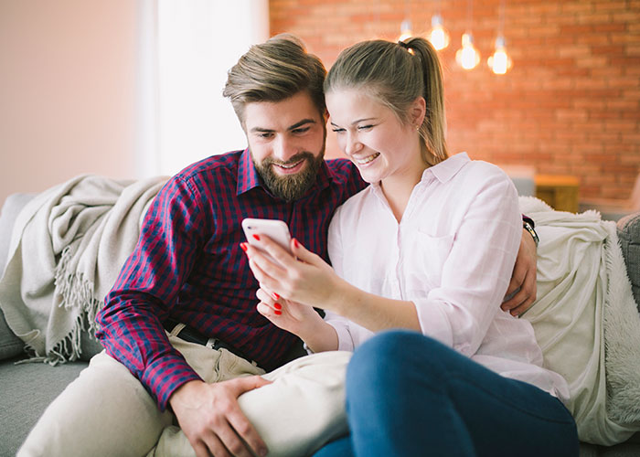 Couple laughing together while looking at a phone, illustrating ridiculous reasons that ended up in the emergency room.