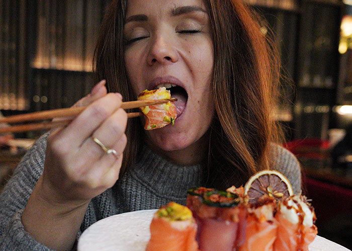 Woman eating sushi with chopsticks indoors, highlighting ridiculous reasons people ended up in the emergency room.