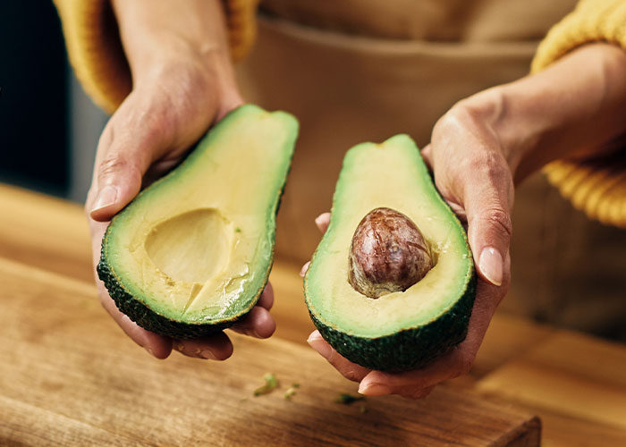 Hands holding a fresh avocado cut in half, illustrating one of the ridiculous reasons people ended up in the emergency room.