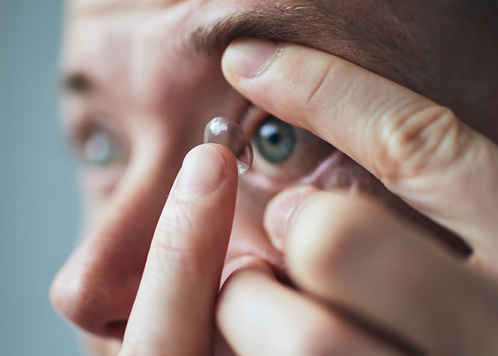 Person carefully placing a contact lens in their eye, illustrating one of the ridiculous reasons ended up emergency room.