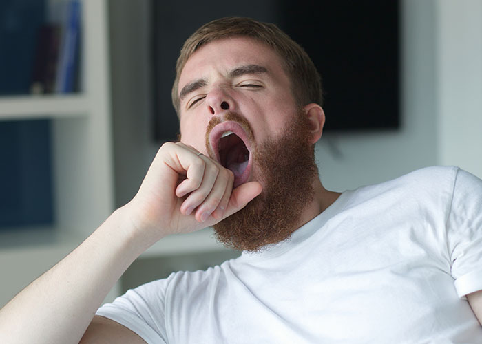 Man with beard yawning widely in casual white shirt, illustrating ridiculous reasons people ended up in the emergency room.