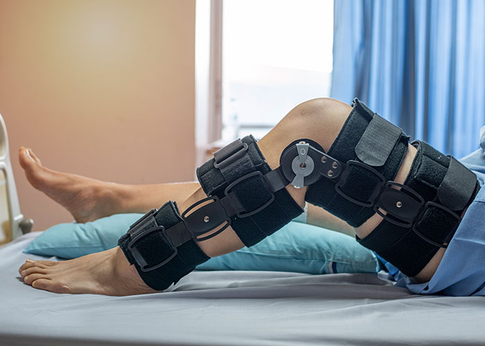 Person lying in hospital bed with a black knee brace, illustrating ridiculous reasons that ended up in the emergency room.