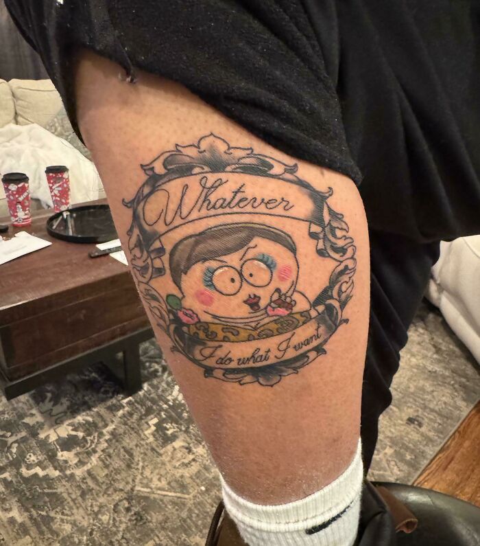 Tattoo fail of a misspelled word and cartoon character on a person's upper leg in a casual home setting.