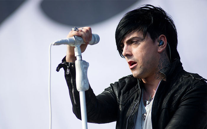 Rock star with dark hair and tattoos singing into a microphone during a live performance on stage.