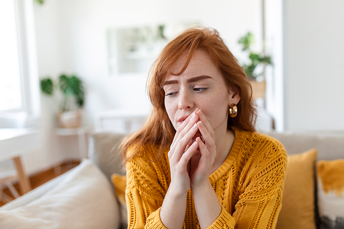 Woman in a yellow sweater sitting indoors, looking pensive and thoughtful, representing couple and tattoo bf ex feelings.