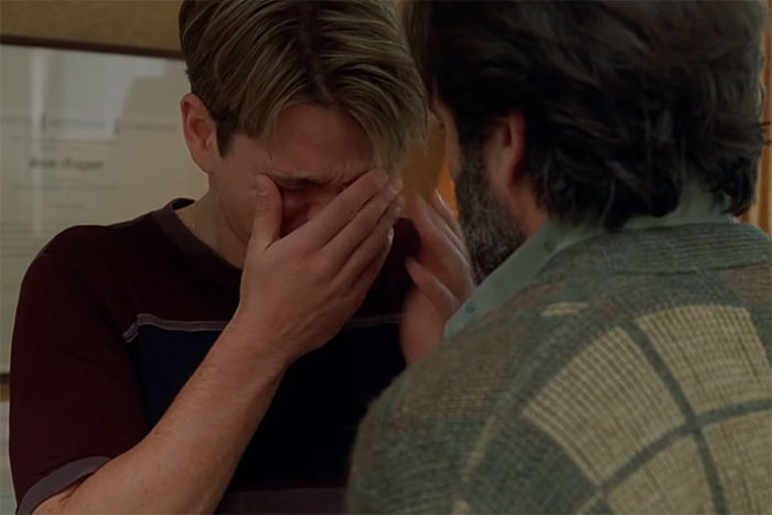 A young man crying and covering his face while talking to an older man, emotional scene from movies that tug at heartstrings.