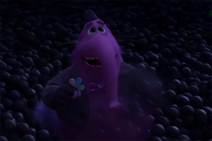 Animated purple elephant character looking emotional, holding a colorful flower, in a dark ball pit scene from movies tugging at heartstrings.
