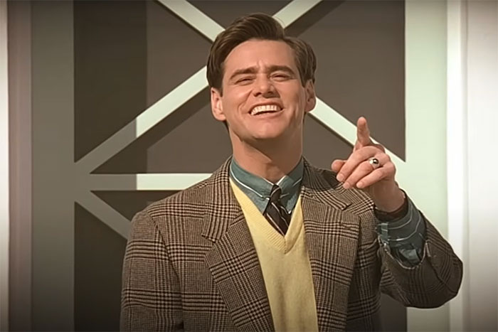 Jim Carrey smiling and pointing in a plaid blazer, green shirt, and yellow sweater vest, representing memorable lines from movies.