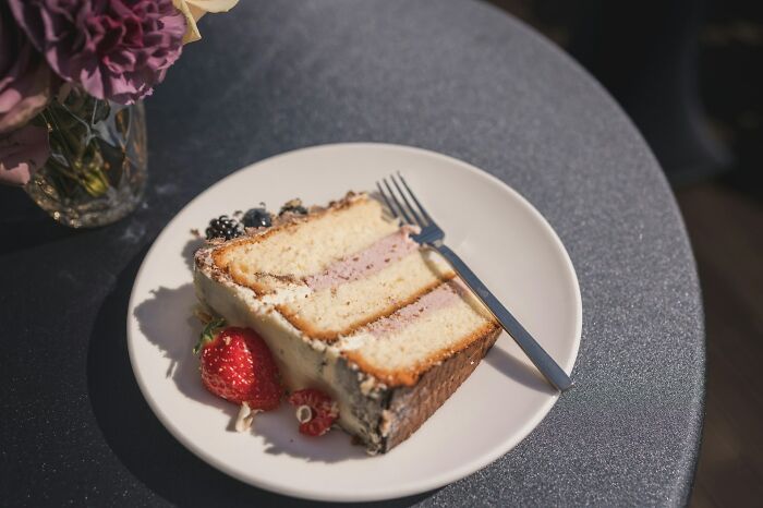 Slice of wedding cake with berries on a white plate at a wedding reception table setting.