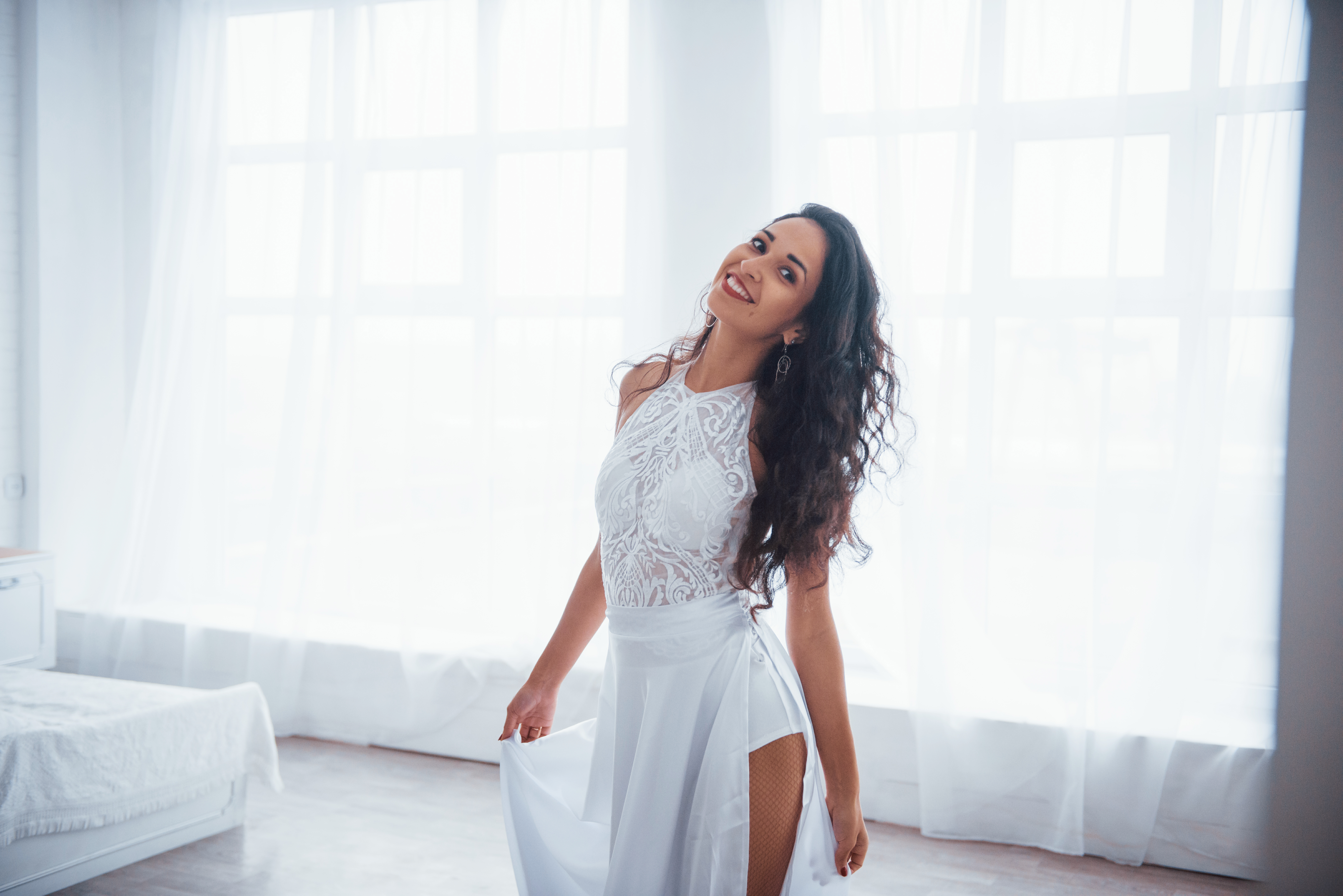 Woman in elegant white dress posing indoors, dressed for a gala with client, capturing a confident and playful moment.