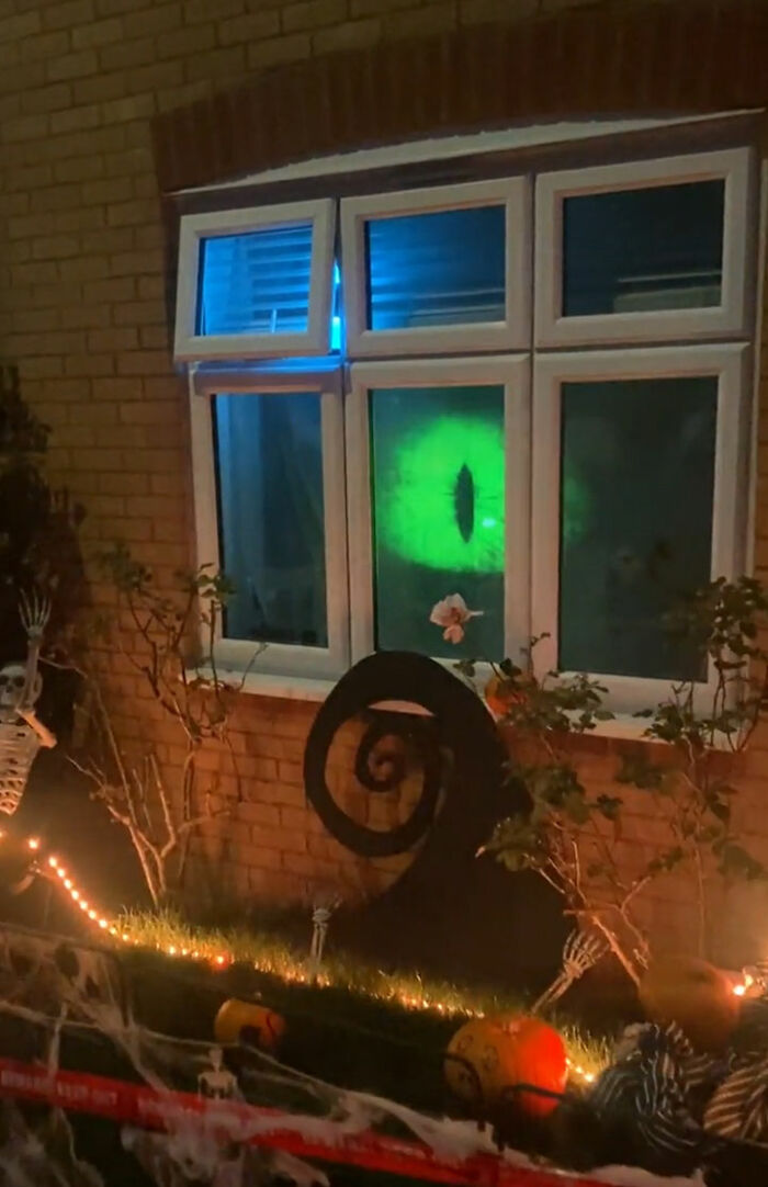 Halloween outdoor decorations with glowing green eye projection on window and skeletons in front yard display at night
