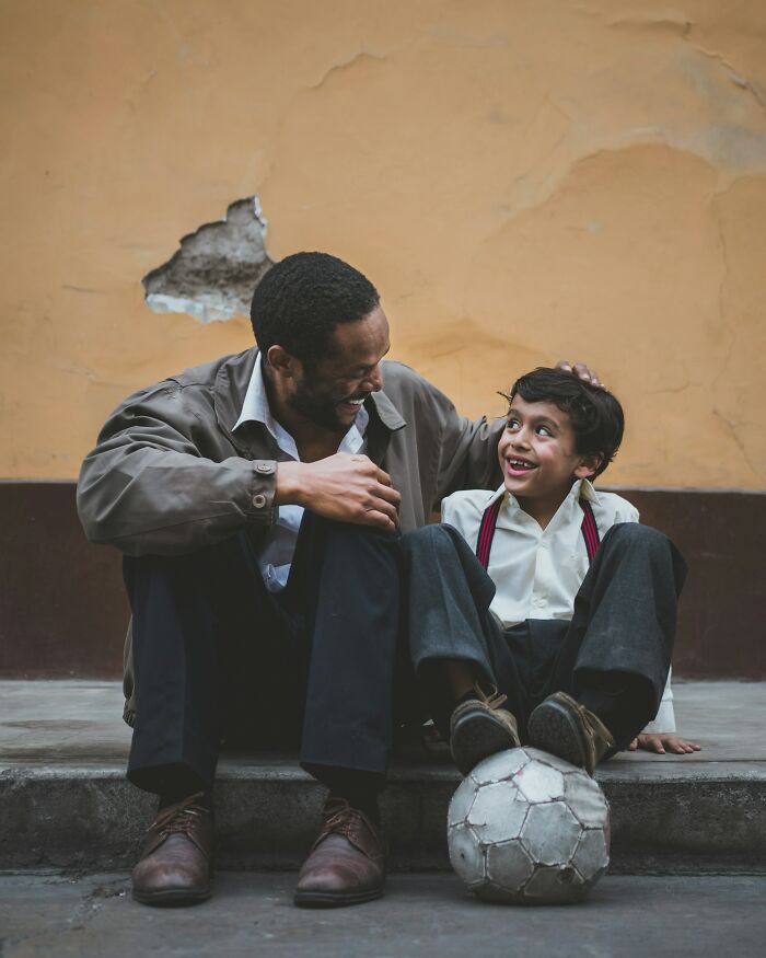 Man and boy sitting on a step with a soccer ball, sharing a joyful moment, reflecting on being disappointed in someone idolized.