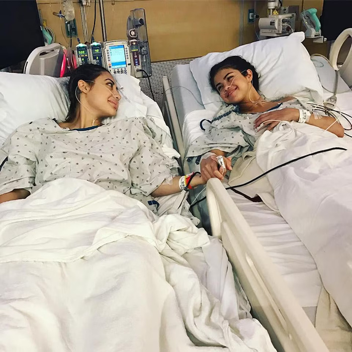 Selena Gomez's kidney donor and Selena holding hands in hospital beds during recovery after surgery. Selena Gomez's kidney donor and Selena holding hands in hospital beds during recovery after surgery.
