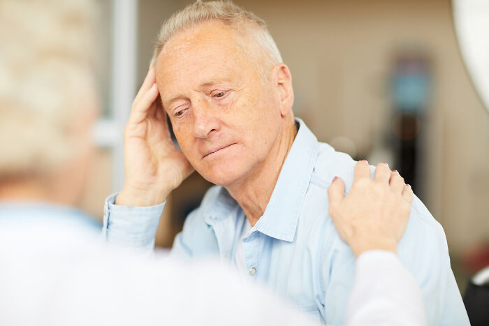 Elderly man in a light blue shirt receiving support from doctor during a difficult medical first opinion consultation.