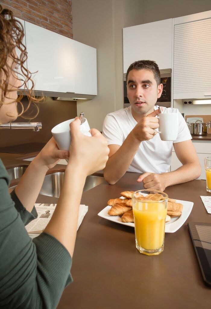 Two people having breakfast in a kitchen, drinking coffee and discussing healthy habits over juice and pastries.