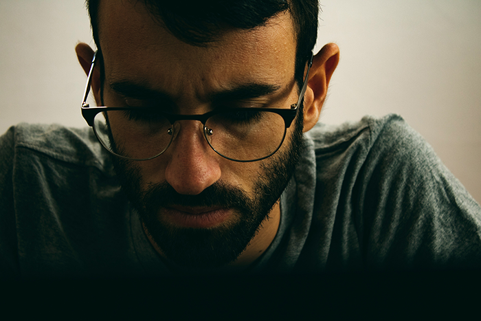 Man with glasses and beard looking down pensively, reflecting on family conflict over lady kissing another man.