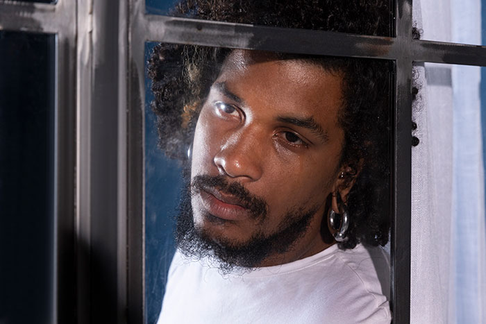 Young man with tear rolling down his cheek, looking out a window, reflecting on learning fianc&eacute;e is in love with her friend.