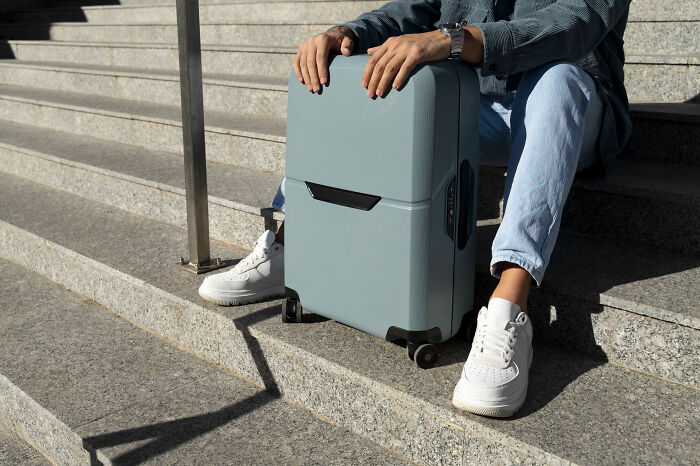 Person sitting on stone steps holding a blue suitcase, illustrating travel loopholes to take advantage of now.