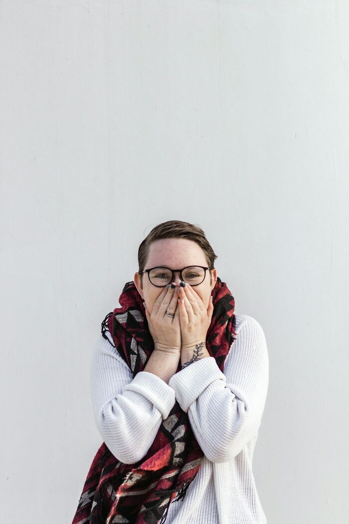 Person wearing glasses and a cozy scarf covering their mouth, showing a moment of embarrassment and awkwardness.