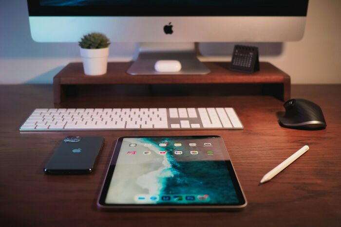 Desk setup with Apple devices including iPad, iPhone, keyboard, and mouse, illustrating technology in workspaces and grudges.