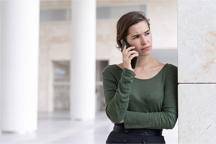 Woman with concerned expression talking on phone, standing indoors, representing sister abandoning autistic brother.